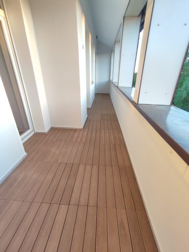 Langer, heller Flur mit Holzfußboden und großen Fenstern.